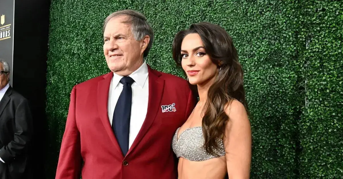 Bill Belichick and Jordon Hudson posing together at a public event, showcasing their relationship